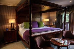 a bedroom with a canopy bed with two chairs and a table at Langshott Manor - Luxury Hotel Gatwick in Horley
