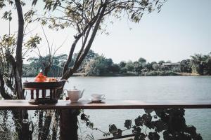 stół z dwoma filiżankami kawy na nim obok jeziora w obiekcie The Antique Riverside Resort w mieście Ban Pong