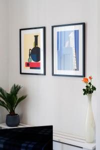 três quadros emoldurados numa parede branca com um vaso com flores em ARCORE Premium Rental Grafton Way em Londres
