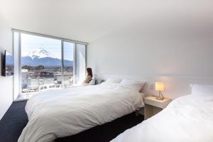 富士河口湖的住宿－THE GARDEN，坐在窗户房间里床边的女人