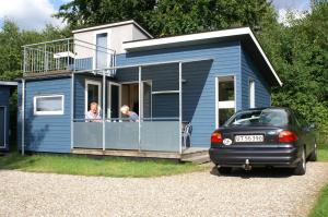 uma pequena casa azul com duas pessoas a olhar pela janela em Fjordlyst Camping & Cottages em Aabenraa
