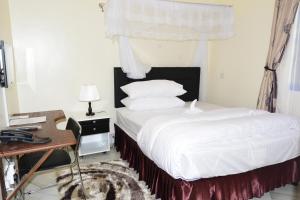 um quarto com uma cama branca, uma secretária e uma janela. em Africa Lodge Arusha em Nkoaranga