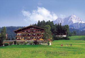 a large building in a field with a mountain at Hotel-Gasthof zur Schönen Aussicht in Sankt Johann in Tirol
