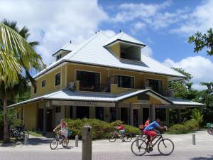 La gente montando bicicletas delante de un edificio amarillo en La Kaz Safran, en La Digue