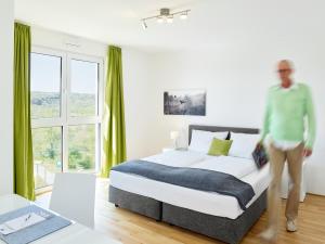 a man standing next to a bed in a bedroom at Aparthotel Parkallee in Mainz