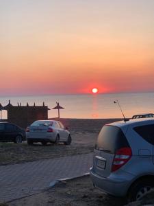 dois carros estacionados na praia com o pôr do sol em Vila Sunrise em Vama Veche