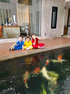 tres niños sentados junto a un estanque con cometas en el agua en The Rest Hotel - ประจวบ en Prachuap Khiri Khan