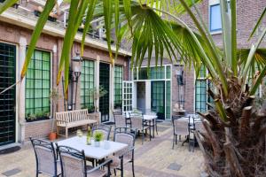 un patio con tavoli, sedie e una palma di Hotel Johannes Vermeer Delft a Delft