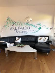 ein Wohnzimmer mit einem schwarzen Ledersofa und einem Tisch in der Unterkunft Alpenglück de Luxe Ferienwohnung am Forggensee in Schwangau