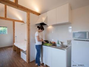 a woman standing in a kitchen preparing food at match guest house（まっちゲストハウス） in Tatsugo