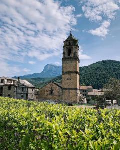 an old building with a clock tower with mountains in the background at Apartamentos Turismo Rural Casa Alfós in Labuerda