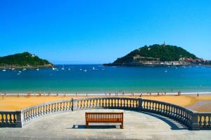 a bench on a beach with people in the water at Hostal Bahía in San Sebastián