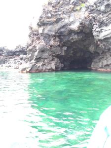 a cave with green water next to a rocky shore at Mandalarose in Catania
