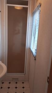 La salle de bains est pourvue d'une douche, d'une fenêtre et d'un lavabo. dans l'établissement AMELAND - Ballum: Stacaravan Chalet (incl. fietsen) bij strand en zee, à Ballum