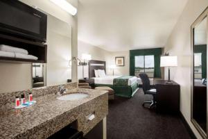 a hotel room with a bed and a bathroom with a sink at Travelodge by Wyndham Livonia in Livonia