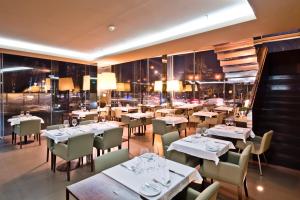um restaurante com mesas e cadeiras brancas e janelas em Golden Tulip São João da Madeira Hotel em São João da Madeira