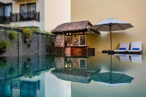 a swimming pool with a table and an umbrella at Silkotel Hoi An in Hoi An