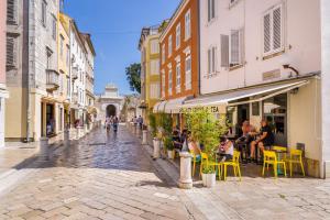 Luxury rooms Zadar old town في زادار: شارع مرصوف بالحصى فيه أشخاص يجلسون على الكراسي في زقاق
