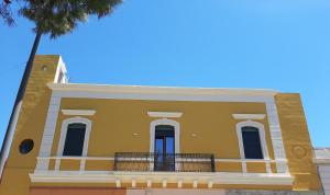un edificio amarillo con balcón y una palmera en Casa vacanze "ALIZZA", en Alezio
