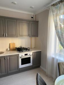 a kitchen with gray cabinets and a stove and a window at 2-ухкомнатная современная новая квартира в центре города in Kostanay
