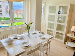 uma mesa branca e cadeiras num quarto com janelas em Apartamento Valdenoja Playa Sardinero em Santander