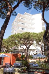 un edificio alto de color blanco con mesas, sillas y árboles en GoettenMar Platja d'Aro, en Platja d'Aro