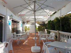 a patio with white tables and white chairs and an umbrella at Pension los Verdiales in La Herradura