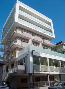 ソットマリーナにあるHotel Jonniのバルコニー付きの白い高い建物、駐車場