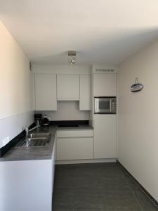 Una cocina blanca con fregadero y microondas. en Karthuizer Zeezicht I, en Nieuwpoort