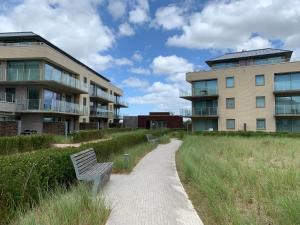 un banco en un camino al lado de un edificio en Karthuizer Zeezicht I, en Nieuwpoort