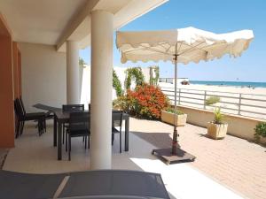 une terrasse avec des tables et un parasol et la plage dans l'établissement Belle villa sur vaste plage Palavas Montpellier, à Palavas-les-Flots