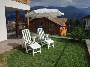 dos sillas blancas y un paraguas en un patio en Villa in Val di Fiemme en Cavalese