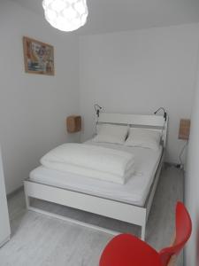 - un lit blanc dans une chambre avec une chaise rouge dans l'établissement Appartement T2 ou T1 côté cour/jardin avec garage, à Rochefort