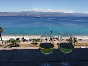 メッシーナにあるThe door of Sicilyのビーチの近くのテーブルに座ったワイン2杯