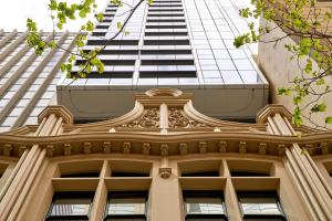 an old building with a tall building in the background at Collins House Apartments by CLLIX in Melbourne