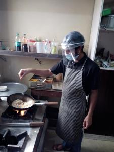 a man in a kitchen preparing food in a wok at Daffodil Delight - Manyata Tech Park in Bangalore