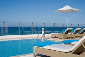 a pool with chairs and an umbrella and the ocean at Althea Kalamies Luxury Villas in Protaras