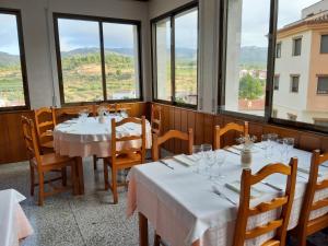 un restaurante con mesas y sillas blancas y ventanas en Ca l'Àngel, en Pinell de Bray