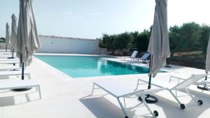 une piscine avec des chaises blanches et des parasols dans l'établissement Il Tramonto Apartment - Villaggio di Mary, à Locorotondo