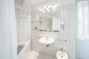 a white tiled bathroom with a sink and a bath tub at Uliveto - Apartment in olive grove directly on the lake in Gargnano