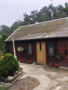 una piccola casa rossa con una porta gialla e fiori rossi di Smiltyne a Klaipėda