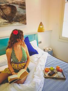 una mujer sentada en una cama leyendo un libro en Hotel Romantic Los 5 Sentidos en Ciutadella
