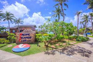 a sign for a resort with a surfboard on the grass at Pacific Islands Club Saipan in Chalan Kanoa