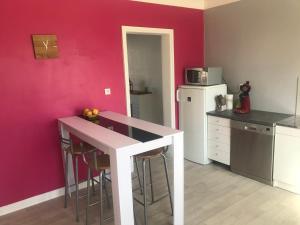 a kitchen with a pink wall and a counter with stools at Gîte Manava - grande maison avec jardin en centre ville in Valognes