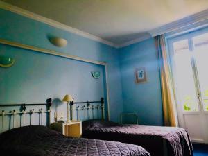 2 camas en un dormitorio con paredes azules y ventana en Le Grand Hôtel en Souillac
