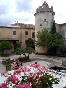 un edificio con una torre e fiori rosa di fronte di L'Auberge Chez Pascal a Saint-Julien-de-Cassagnas