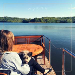 a woman sitting on a boat with a dog at wySPA Kaszuby-domki na wodzie in Ostrzyce