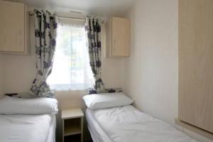Cette petite chambre comprend 2 lits et une fenêtre. dans l'établissement Edinburgh - Seton Sands - Rio Caravan - Pet Friendly, à Édimbourg