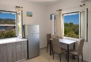 a kitchen with a table and a refrigerator and two windows at Boursinos cozy apartments in Lefkada