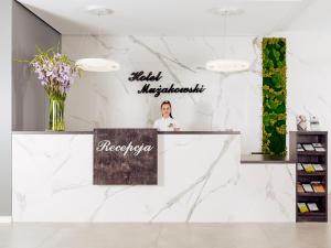 a woman standing at a counter in a white marble lobby at Hotel Mużakowski in Łęknica